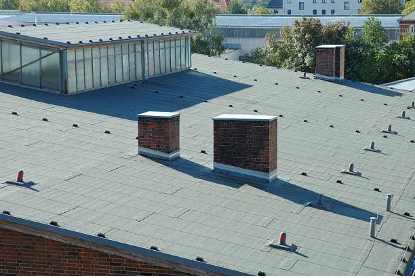 Flat commercial roof with a gray membrane surface, vent pipes and two brick chimneys