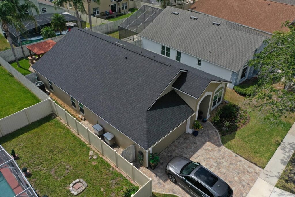 Aerial view of a single-story home with a dark gray shingle roof, a paver driveway and a fenced back yard