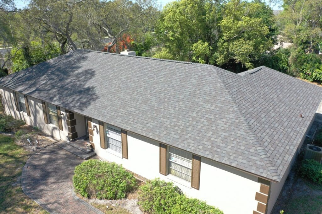 Aerial view of a single-story home with a gray shingle hip roof and trimmed shrubs along the front