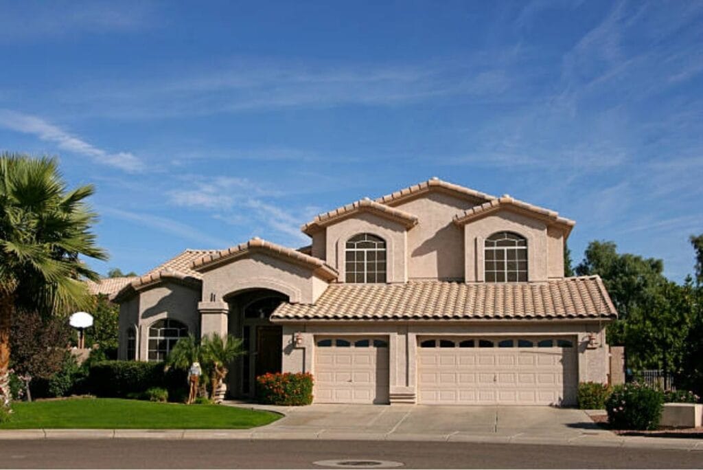 Two-story stucco home with a light tan tile roof, palm trees and a three-car garage