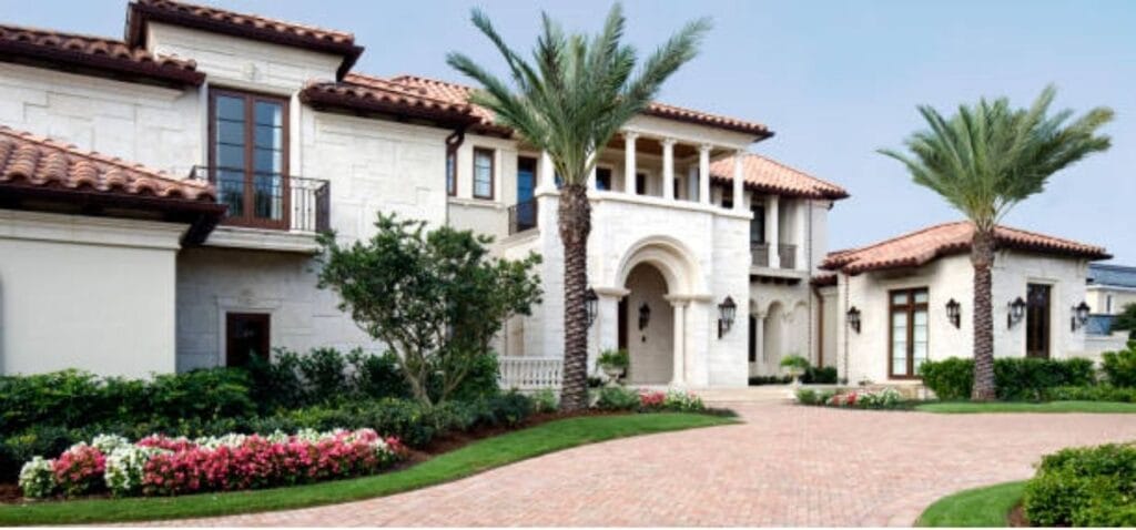 Two-story Mediterranean-style home with a red clay tile roof, palm trees and a brick paver driveway