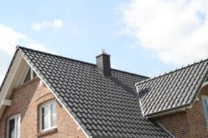 Dark glazed tile roof with a dark chimney and brick house walls under a partly cloudy sky