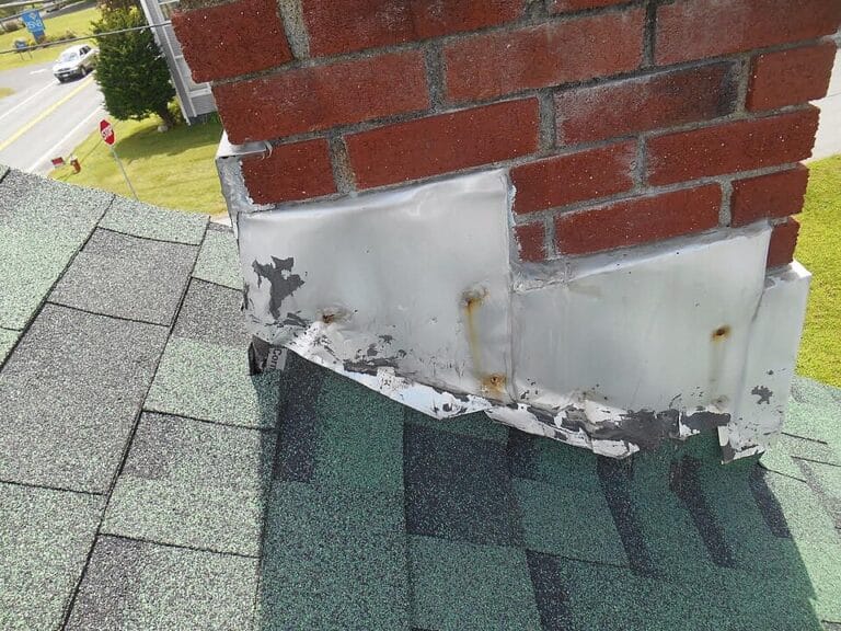 Metal flashing peeling away from the base of a brick chimney on a shingle roof