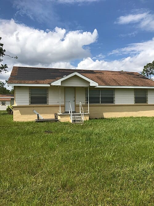 Single-story house with dark patches where wind tore shingles off the roof